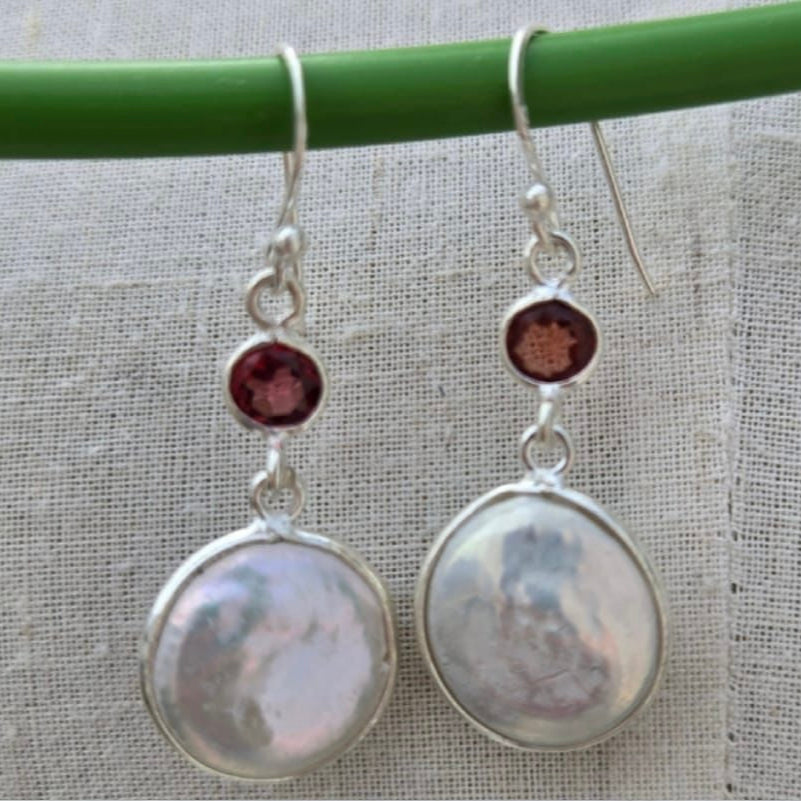 Pair of silver earrings with round stones on a green stick against a textured fabric background