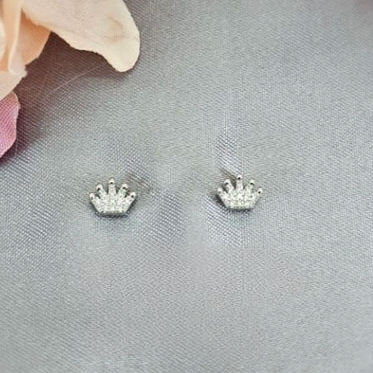A pair of sterling silver crown-shaped stud earrings with cubic zirconia embedded in the design, displayed against a floral backdrop.