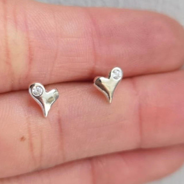 Heart-shaped silver earrings with clear stones on a hand