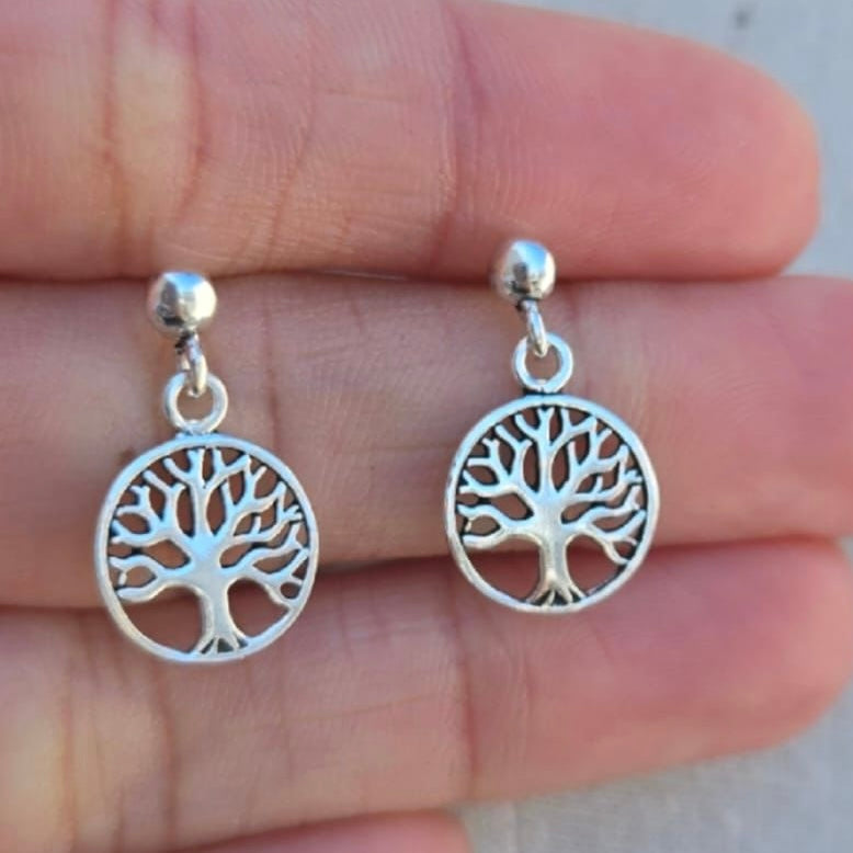 Silver tree-shaped earrings held between fingers against a neutral background