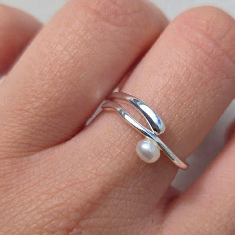 Silver ring with a pearl on a finger against a neutral background