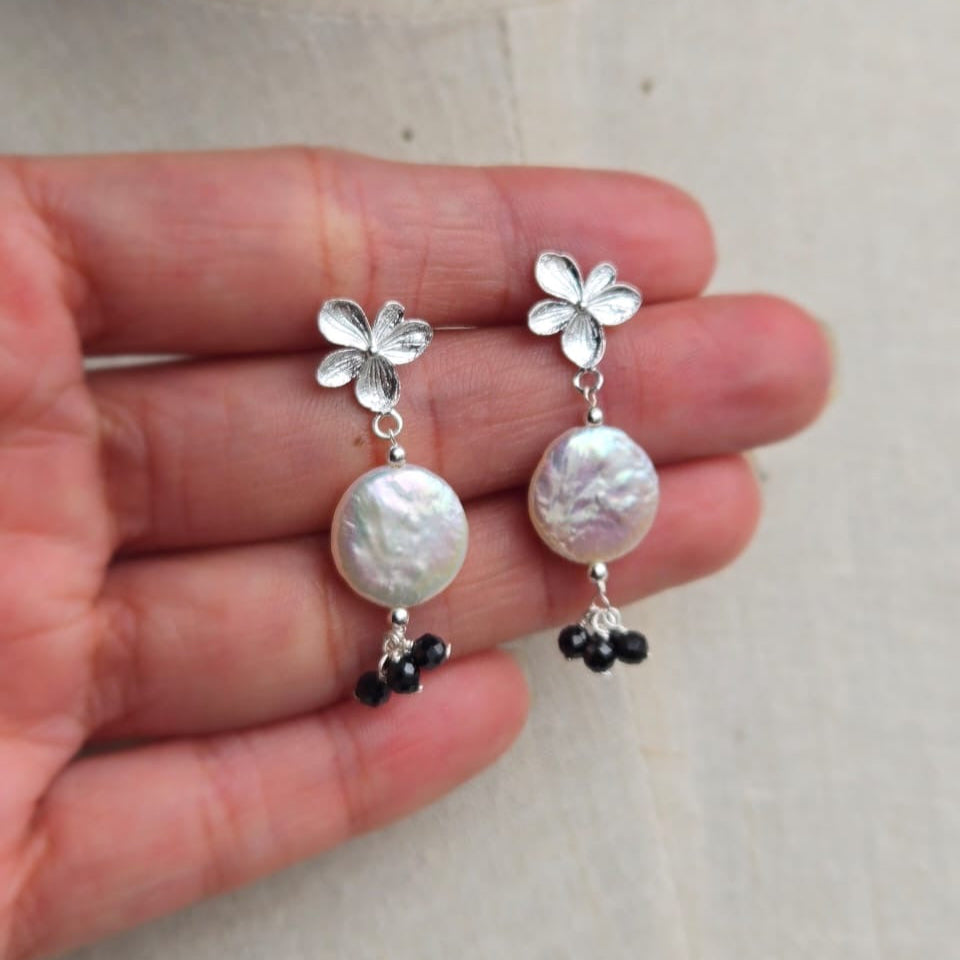 Silver earrings with pearl and black bead details held between fingers on a neutral background