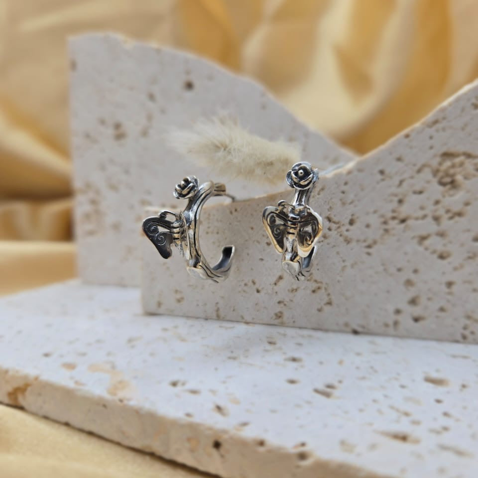Pair of silver earrings on a stone display block with a soft yellow background