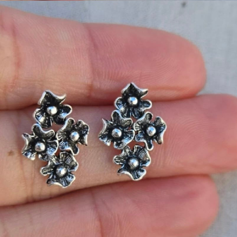 Silver floral earrings held between fingers against a neutral background