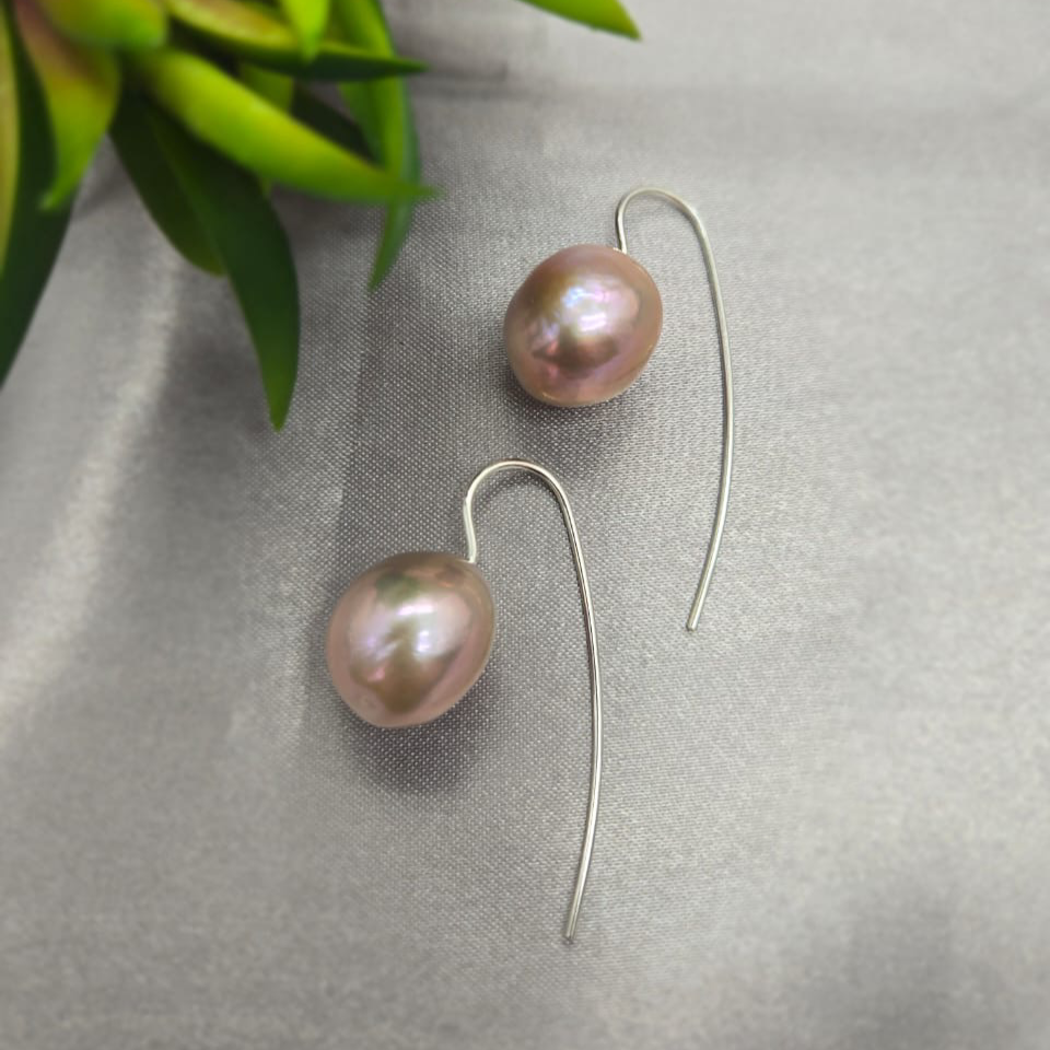 Pair of pink pearl earrings on a gray surface with green leaves in the background