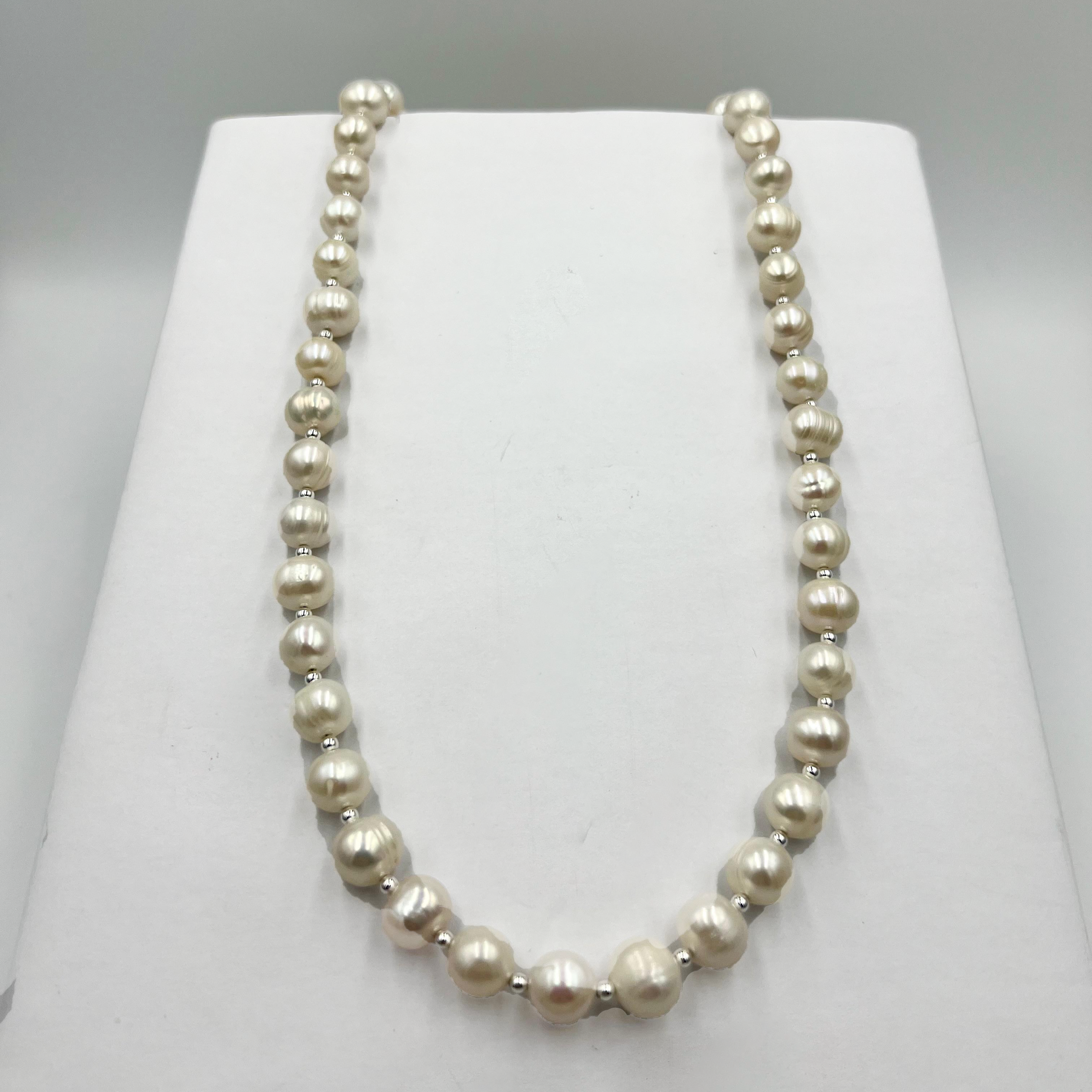 A white pearl necklace with sterling silver small ball links displayed on a white stand.