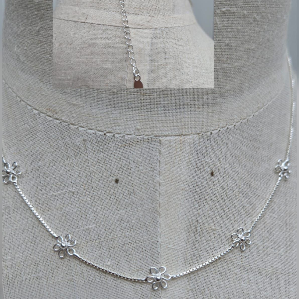 Silver necklace with floral pendants on a mannequin bust.