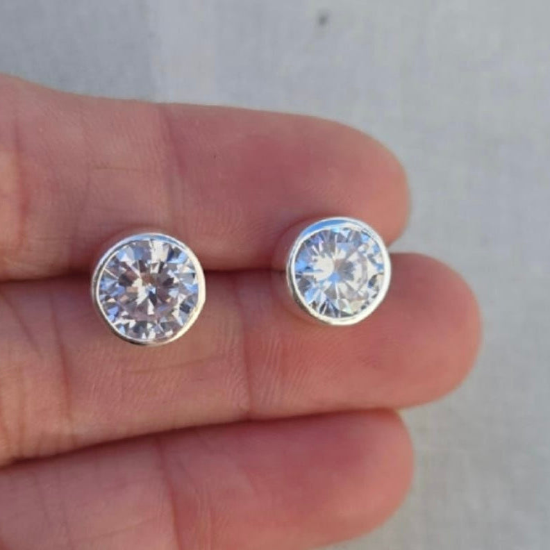 Silver stud earrings held between two fingers against a neutral background