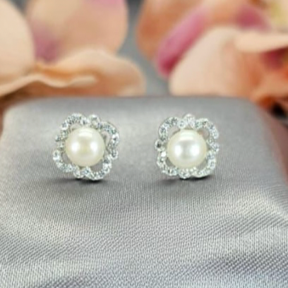 A pair of sterling silver stud earrings with pavé cubic zirconia detail, displayed on a textured background with flower petals scattered around.