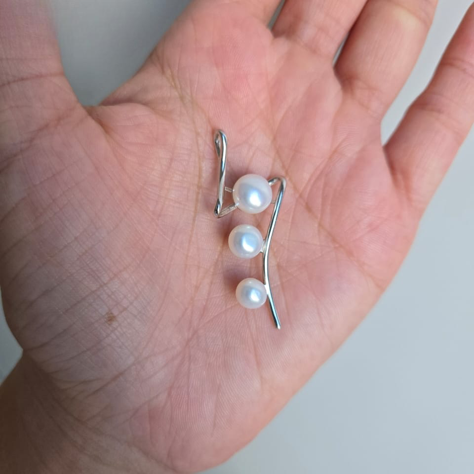 A sterling silver pendant with three freshwater pearls held in a person's hand.