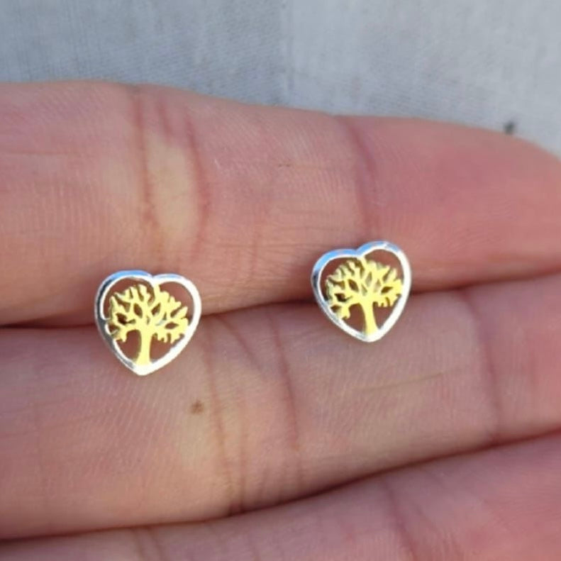 Heart-shaped earrings with tree design held between fingers on a neutral background