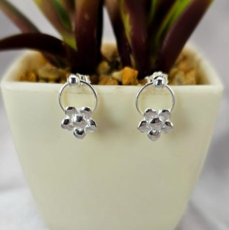 A pair of sterling silver stud earrings with a floral design on a hoop, displayed in front of a potted plant.