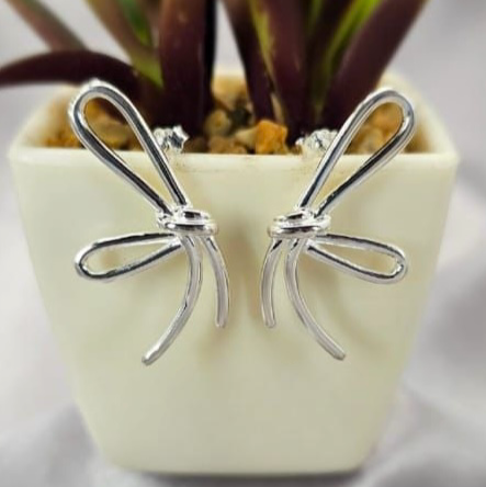 A pair of sterling silver large bow studs earrings displayed in front of a potted plant.