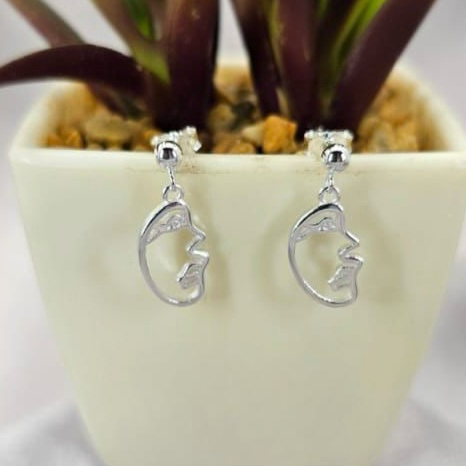 A pair of sterling silver face stud earrings displayed in front of a potted plant.