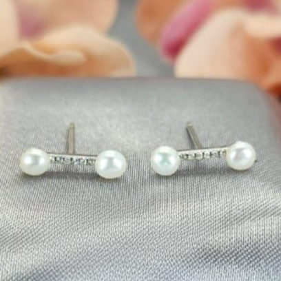 A pair of sterling silver stud earrings featuring freshwater pearls, displayed on a textured surface with a floral background.