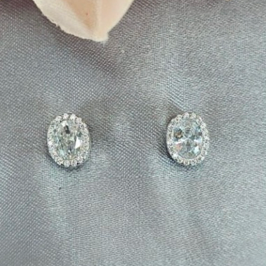 A pair of sterling silver and cubic zirconia oval stud earrings displayed on a fabric surface, with a pink floral petal in the background.