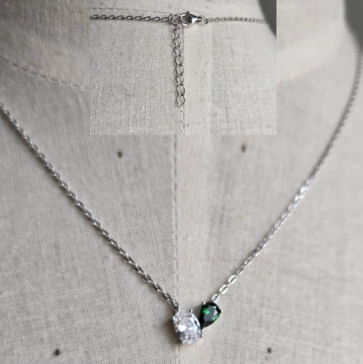 Necklace with a green gemstone and clear stone on a light gray background
