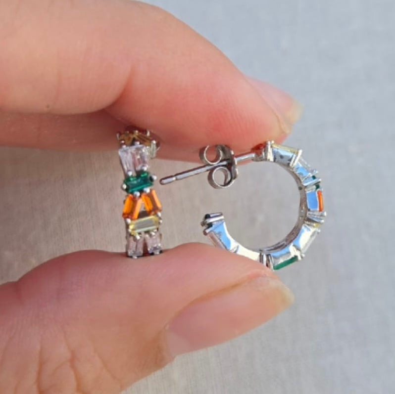 Close-up of two pairs of earrings held between fingers against a neutral background