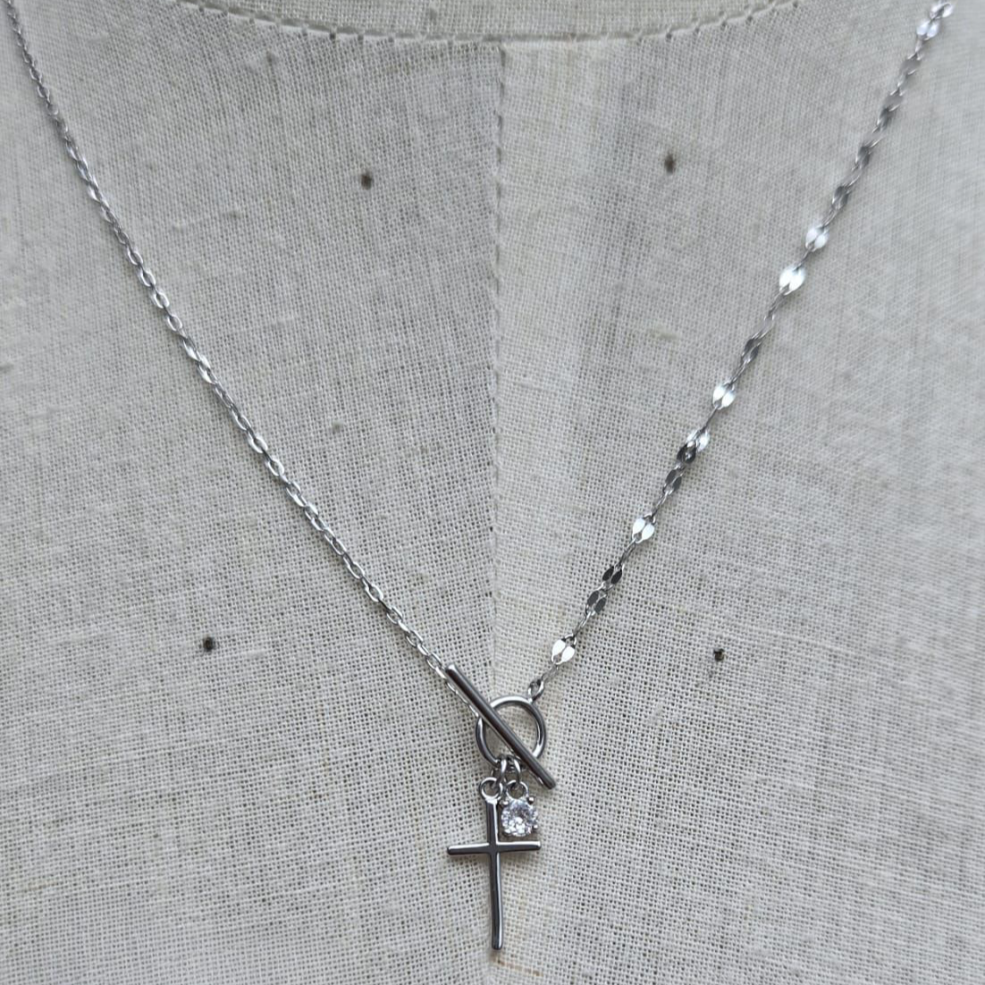 Silver necklace with a cross pendant on a gray fabric background