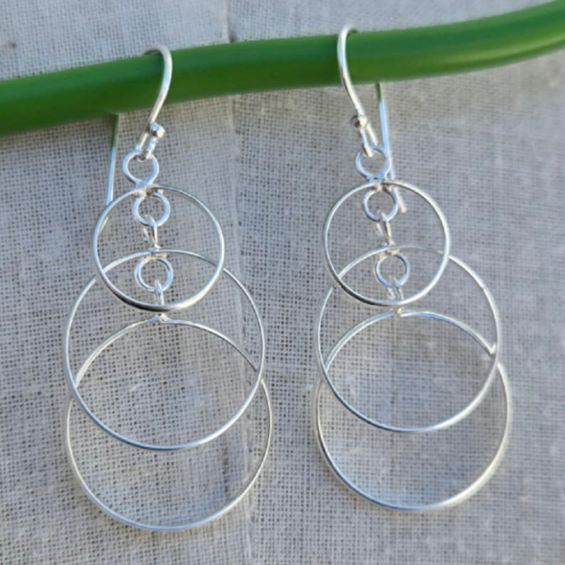 Genuine sterling silver hoop earrings hanging on a green stick against a grey background