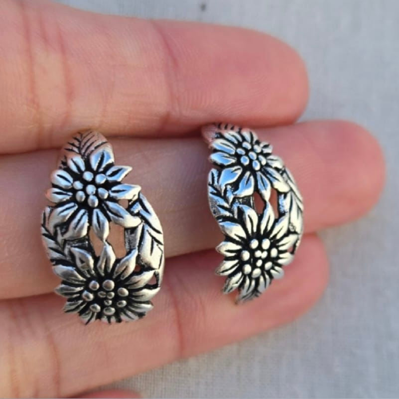 Silver floral hoop earrings held between fingers against a neutral background