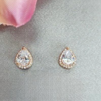 A pair of teardrop-shaped cubic zirconia earrings with rose gold plating, displayed against a neutral background with a pink floral element.