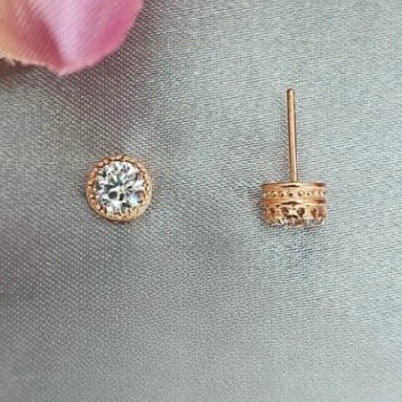 Rose gold stud earrings on a gray surface with a pink flower in the background
