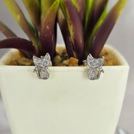 A pair of sterling silver kitten stud earrings with cubic zirconia pavé, displayed in a white pot with purple plants in the background.