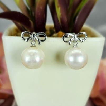 A pair of sterling silver earrings with freshwater pearls, displayed in a white vase with a green plant in the background.