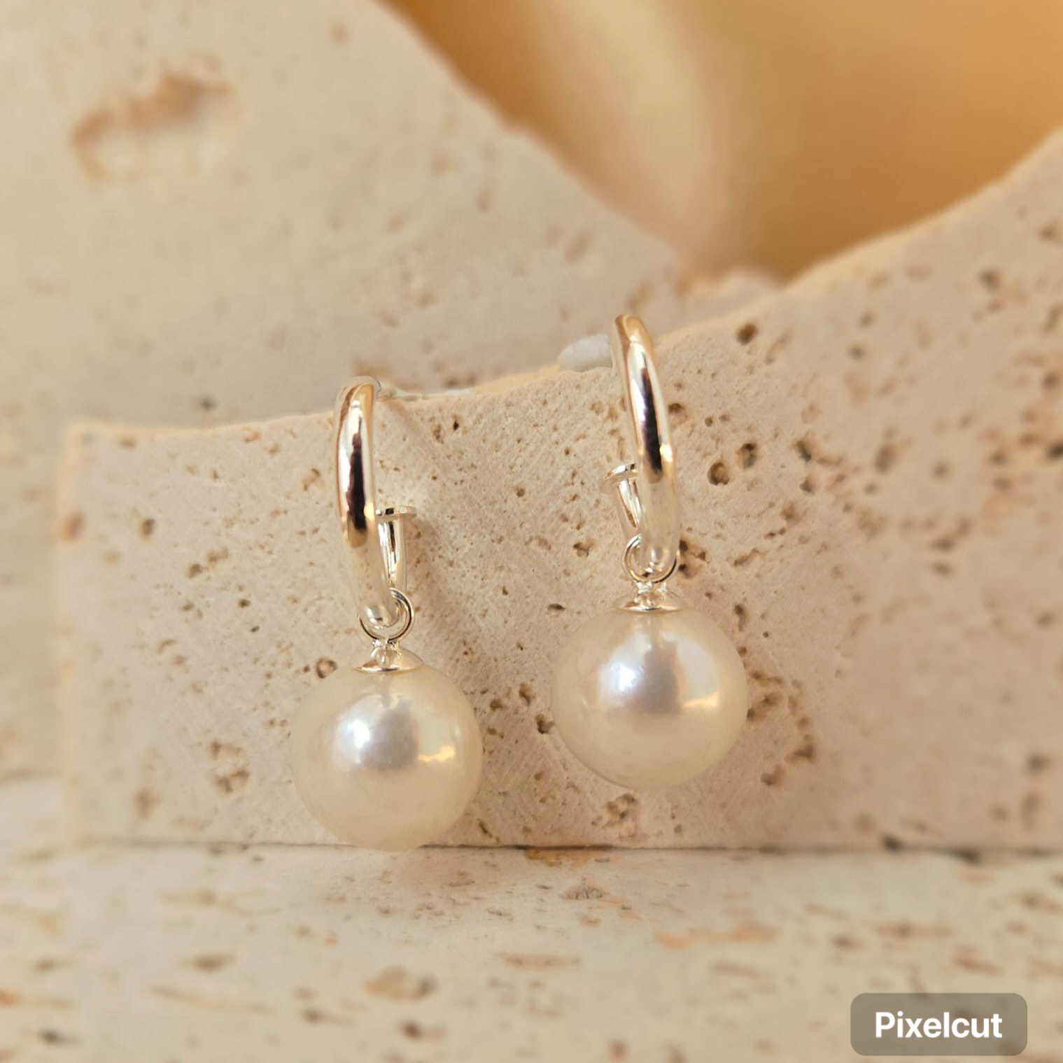 Pearl earrings with gold hooks on a textured beige surface
