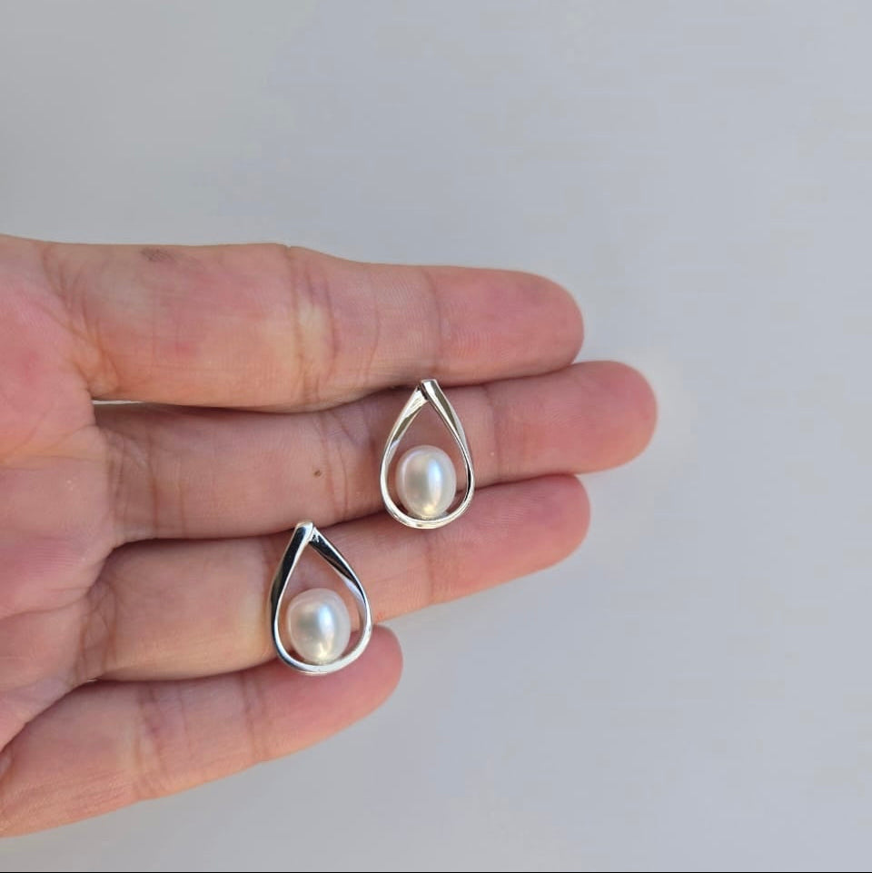 A pair of teardrop-shaped sterling silver stud earrings with freshwater pearls in the center, held between fingers against a plain background.