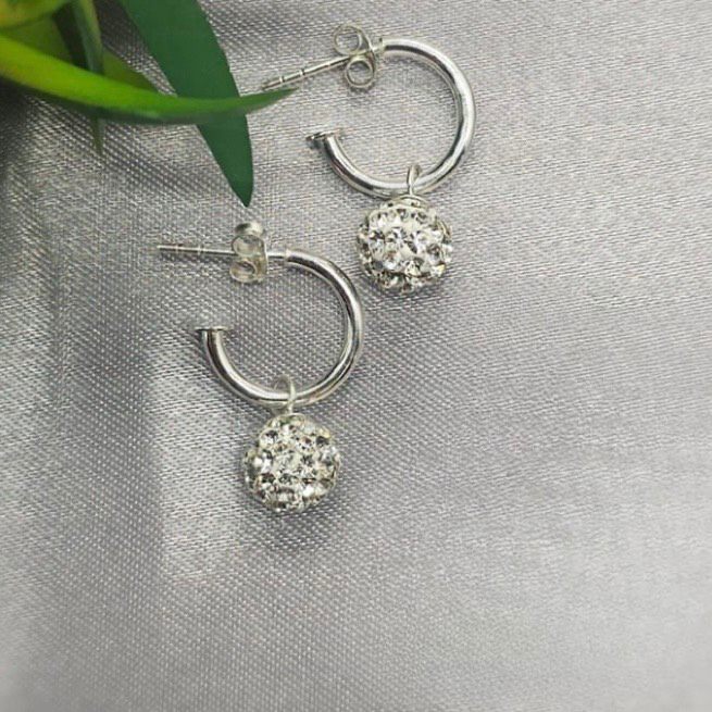 A pair of sterling silver hoop earrings with bling disco ball cubic zirconia embellishments, displayed against a grey background with a green leaf.