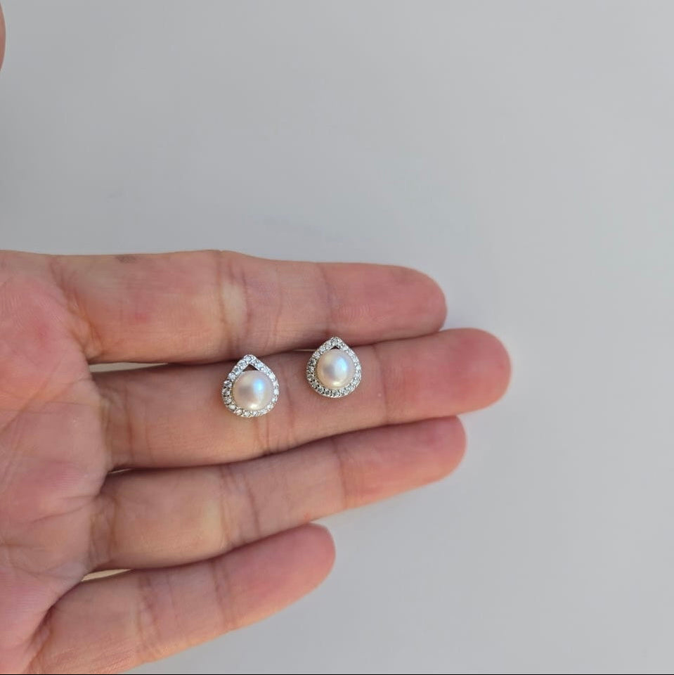A pair of sterling silver teardrop-shaped earrings with freshwater pearls and cubic zirconia accents, displayed on a hand.