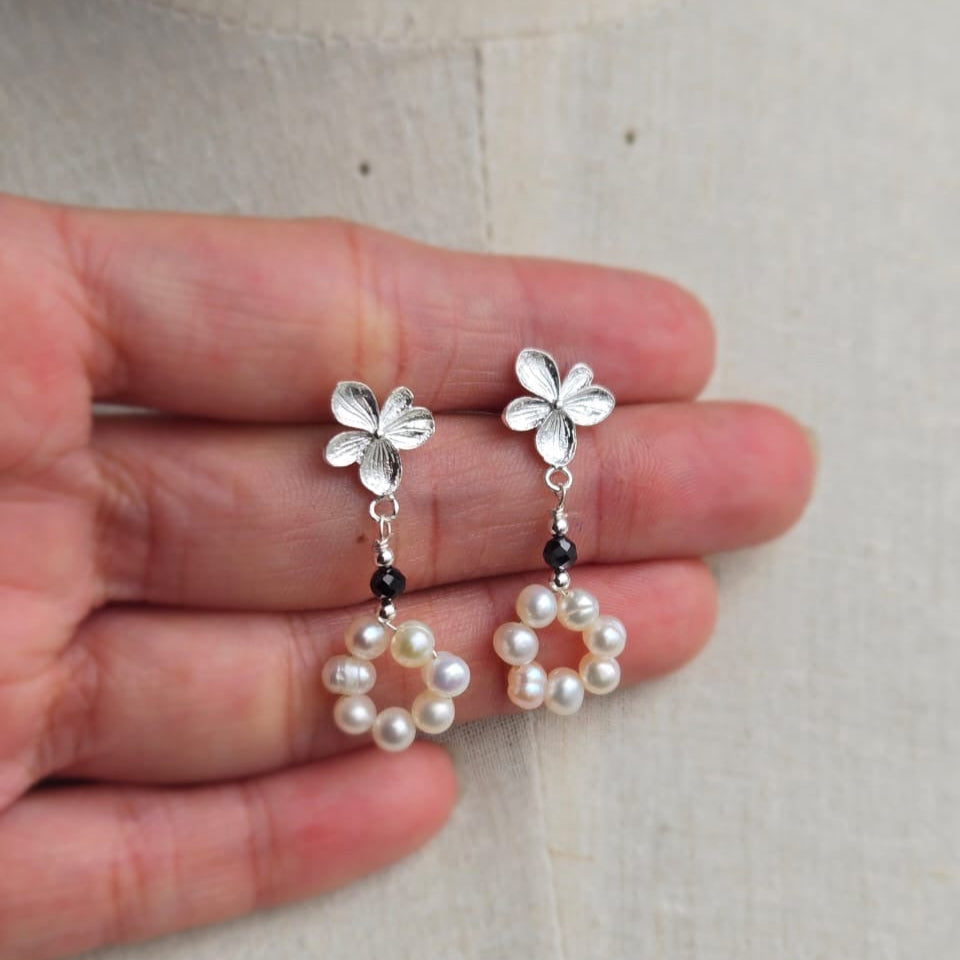Flower-shaped earrings with pearl drops held between fingers on a light background