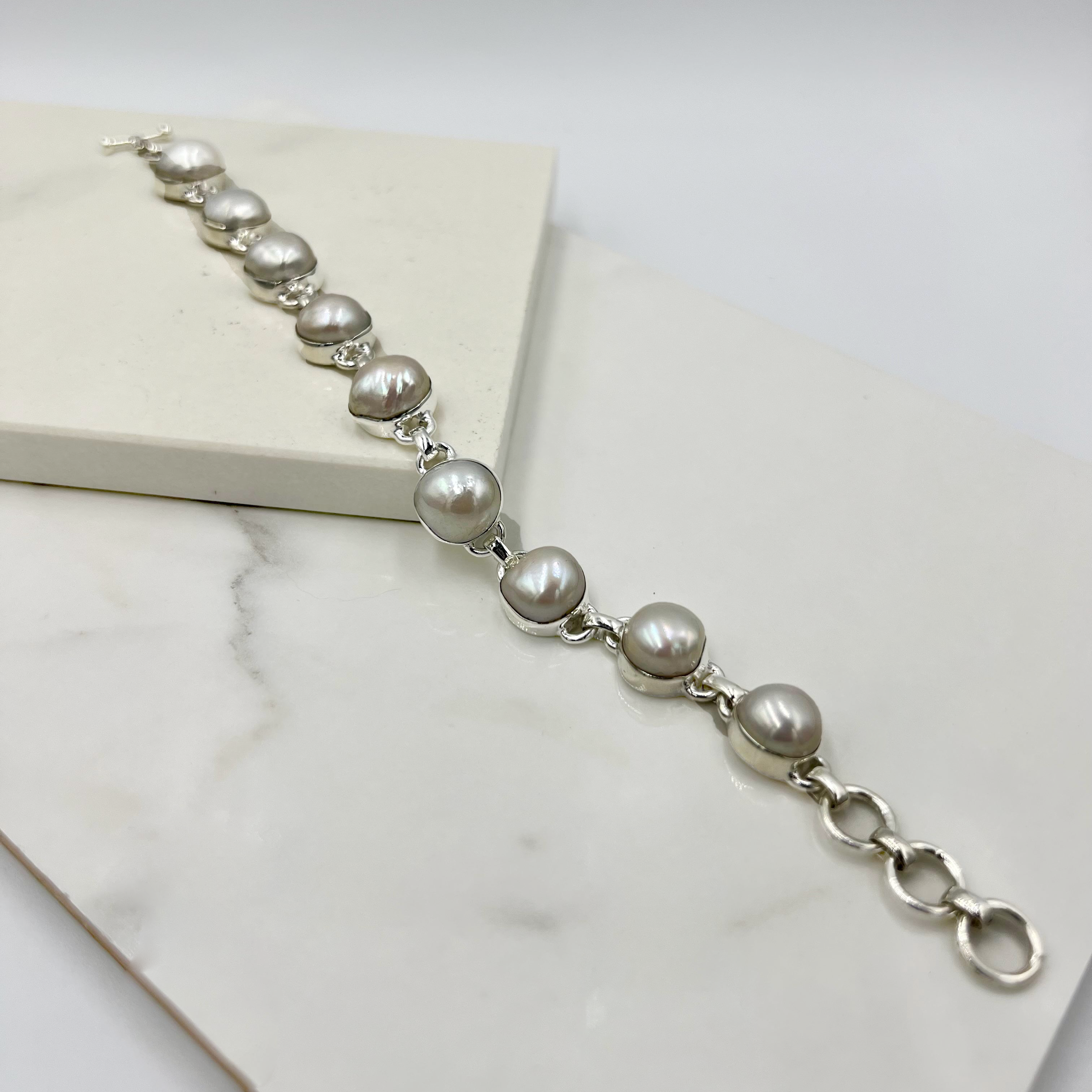 A silver pearl bracelet laid out on a white surface.