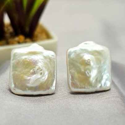A pair of square rough freshwater pearl stud earrings on a textured surface.