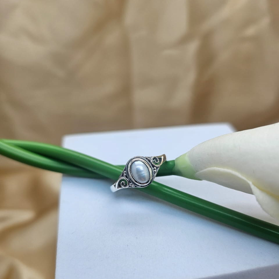 Silver ring with a pearl on a white flower against a beige background