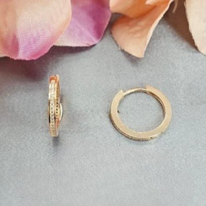 Gold hoop earrings on a light gray surface with pink flowers in the background