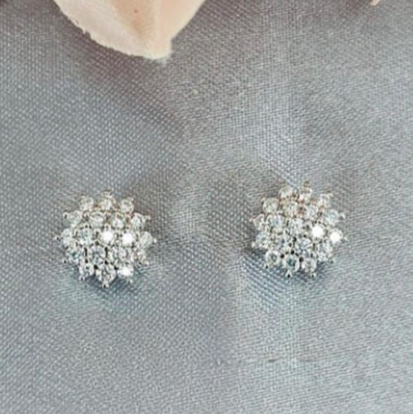 A pair of cubic zirconia cluster studs on a gray background, with the earrings positioned upright and glistening with light.