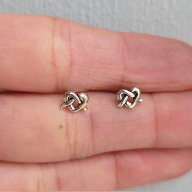 Pair of knot-shaped earrings held between two fingers on a neutral background