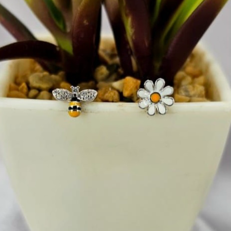 Stud earrings with a cute bee and flower design, placed in a white pot with a green plant.