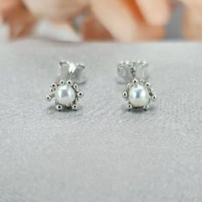 A pair of petite freshwater pearl stud earrings with a clasp detail, made of sterling silver, displayed on a textured surface.