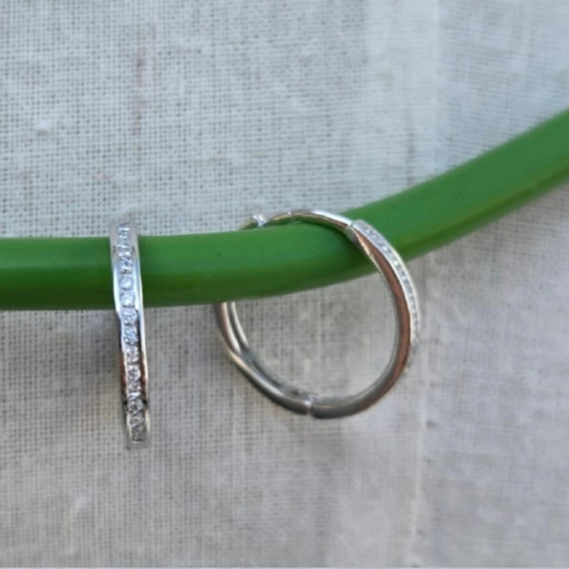 Silver hoop earrings on a green stick against a gray background