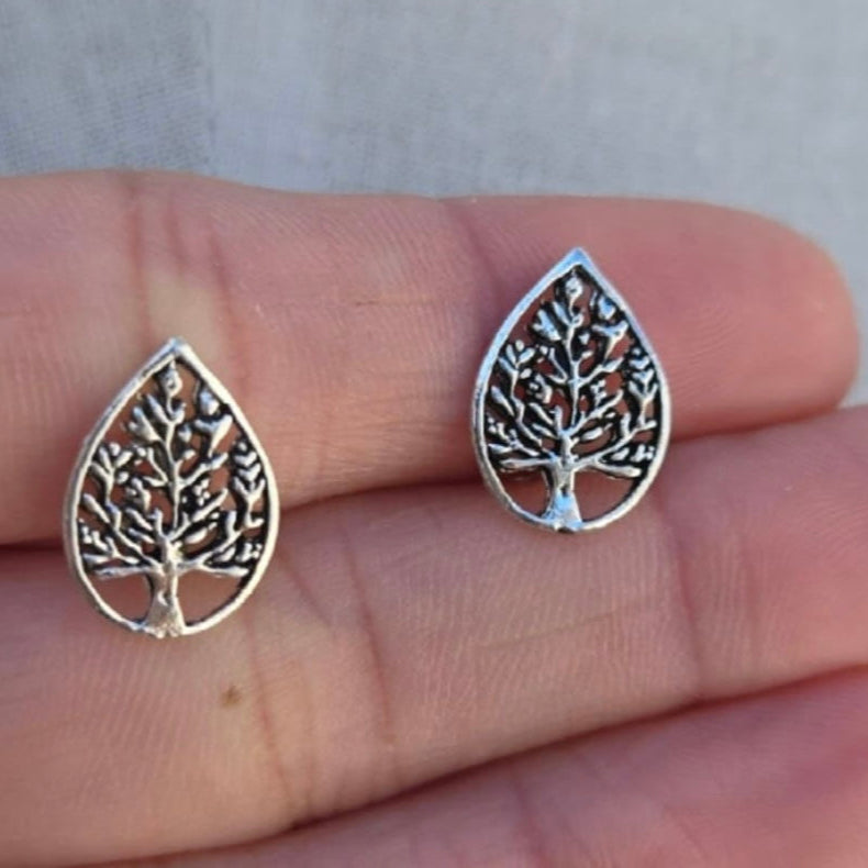 Silver tree-shaped earrings held between fingers against a neutral background