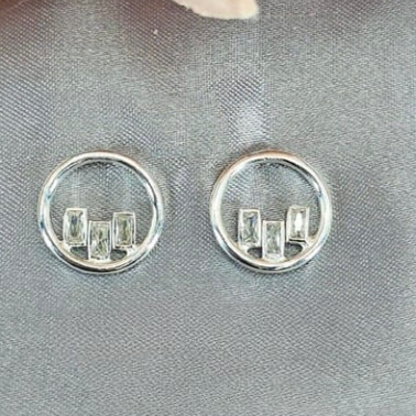 A pair of sterling silver round studs with cubic zirconia rectangular drops on a grey background with a floral pattern.