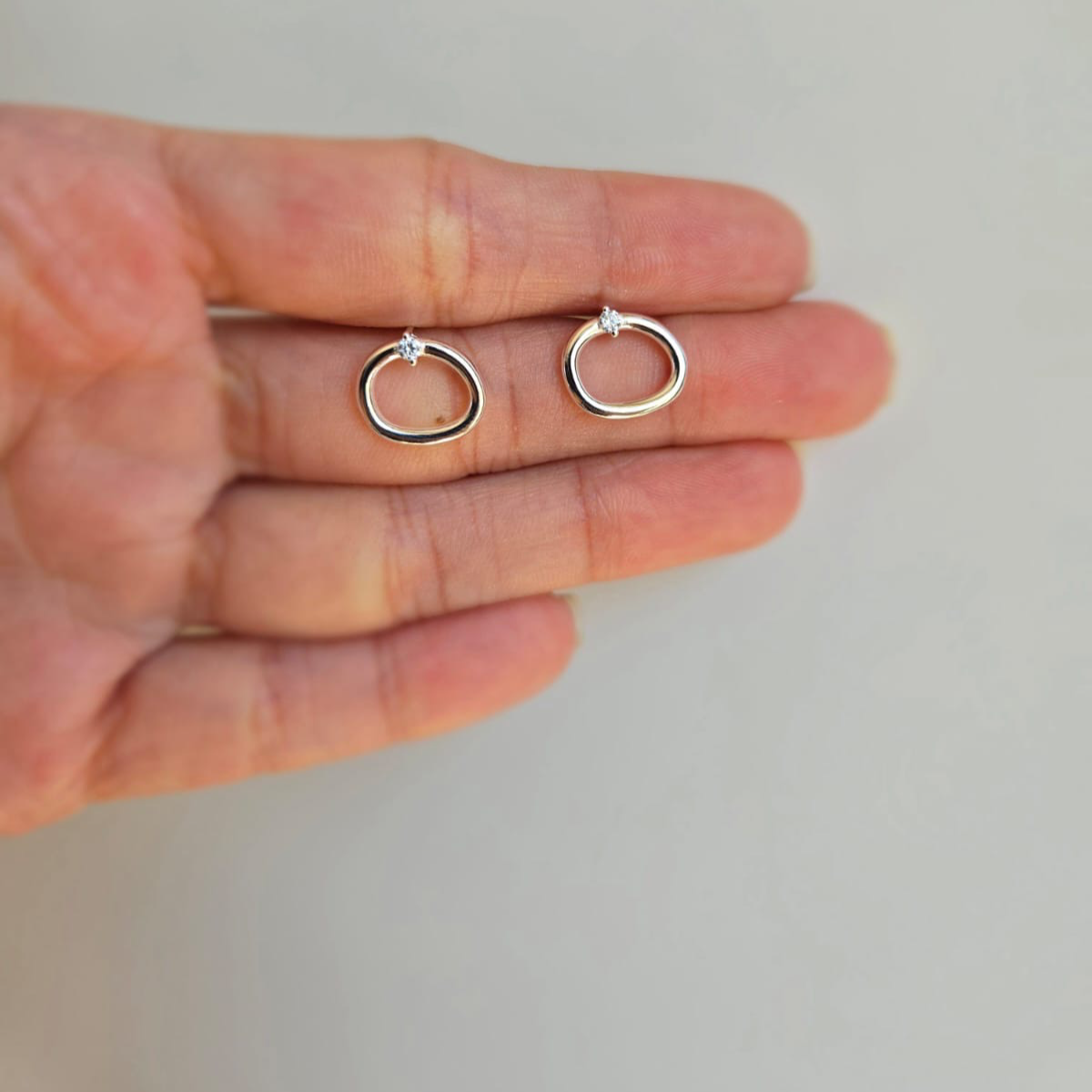 A pair of sterling silver open oval stud earrings with cubic zirconia, displayed on a hand.