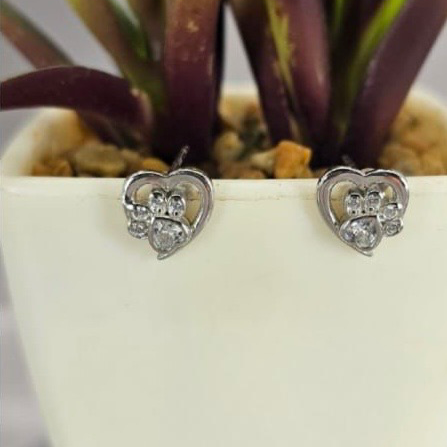A pair of sterling silver heart-shaped stud earrings with cubic zirconia details, displayed against a white plant pot background.