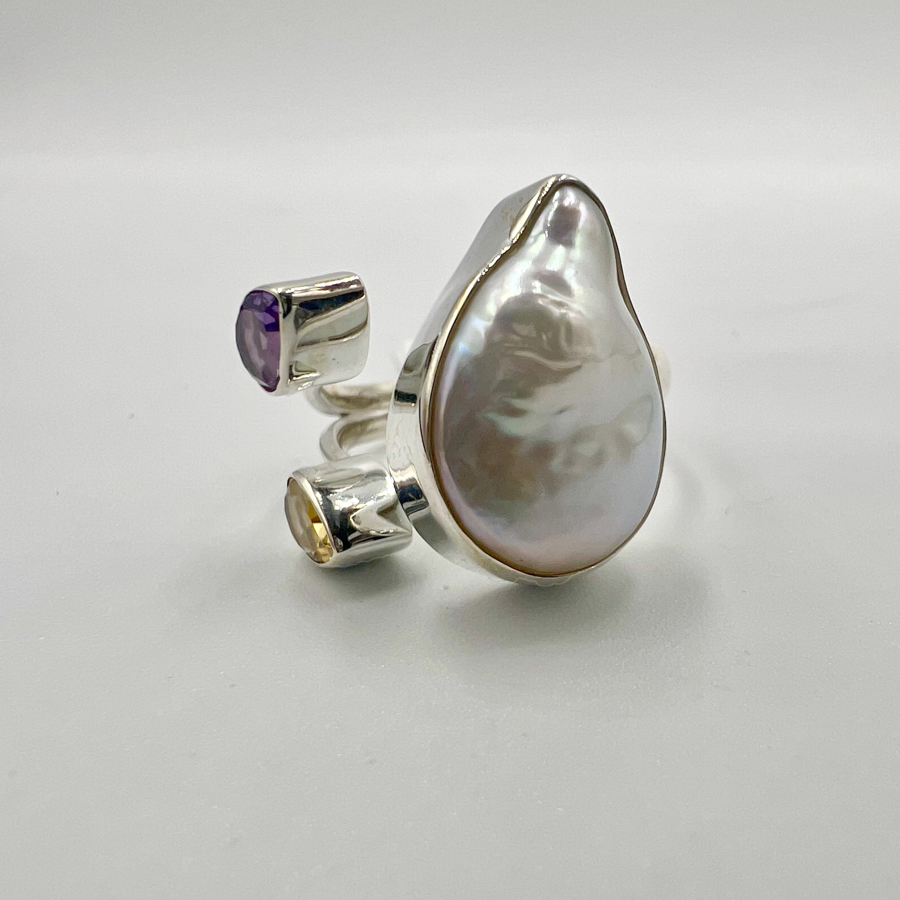 A sterling silver ring with a large pearl and two semi-precious stones, featuring an open band design.