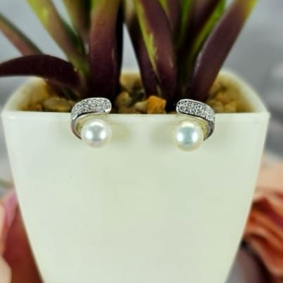 A pair of sterling silver stud earrings with pavé and freshwater pearls, displayed in a white vase with a green plant.
