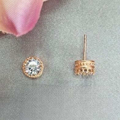 Rose gold earrings with clear gemstones on a gray surface.